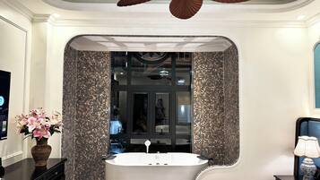 Une salle de bain moderne avec une baignoire sur pieds, un ventilateur de plafond et un vase décoratif posé sur le meuble-lavabo.