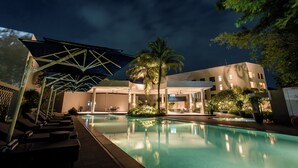 A pool area with lounge chairs, a covered seating area, and a building with multiple windows.