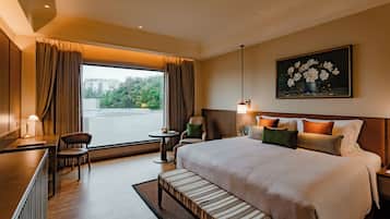 A hotel room with a large bed, a desk, a chair, a small table, and a painting on the wall.