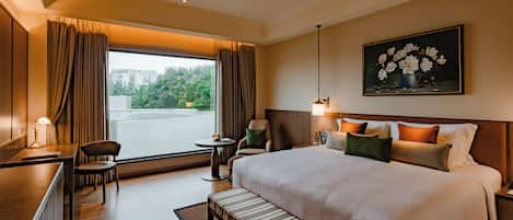 A hotel room with a large bed, a desk, a chair, a small table, and a painting on the wall.