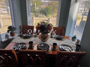 Une table à manger dressée pour quatre personnes, avec un vase de fleurs, des assiettes, des couverts et des verres.