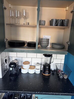 Une cuisine équipée d’une machine à café Bosch, d’un mixeur et de bocaux étiquetés pour conserver le thé, le café et le sucre.