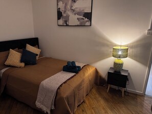 Ein Schlafzimmer mit einem Bett, Kissen, einer Nachttischlampe, einem Wandbild und Holzboden.