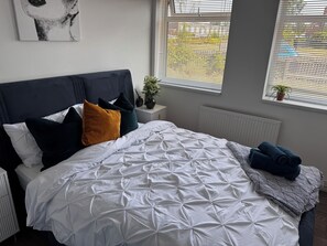 Un lit avec une couette blanche, plusieurs oreillers et une couverture.