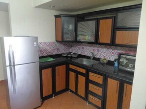 A compact kitchen with a stainless steel refrigerator, wooden cabinets, a tiled backsplash, and a black countertop. - BeSt PorTo GolF MarIna Chalet (Marsa Matrouh Governorate)