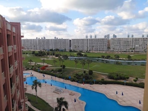 A hotel with a swimming pool, a golf course, and a view of high-rise buildings. - BeSt PorTo GolF MarIna Chalet (Marsa Matrouh Governorate)