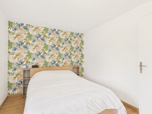 Una camera da letto con un letto, una testiera in legno e una parete decorata con un motivo a foglia tropicale.