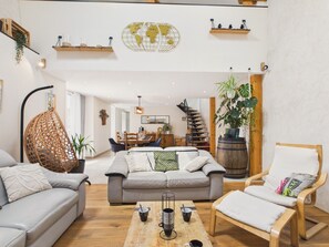 A spacious living area with a sofa, chairs, a coffee table, and a wooden barrel. There is a hanging chair and a staircase leading to another room. - Quiet house with large garden - 7 guests (Plouguerneau)