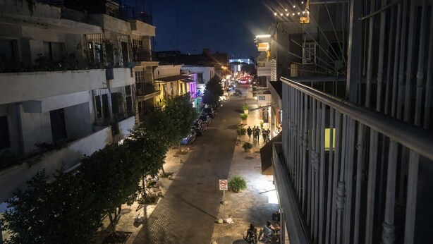A nighttime street view with buildings, a paved road, and a few pedestrians. - Room-balcony Street View Bedroom Zona Co (Santo Domingo)