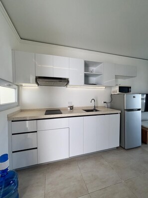 Eine moderne Küche mit weißen Schränken, einem Edelstahl-Kühlschrank, einer Mikrowelle und einem eingebauten Backofen.