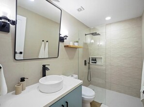 Casa de banho moderna com lavatório branco, torneira preta e cabine de duche com parede de vidro.