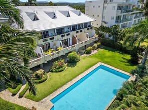 Um hotel de vários andares com piscina, rodeado por relvados bem cuidados e palmeiras.