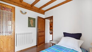 Une chambre à coucher avec un lit, un radiateur, une porte en bois, un miroir et une fenêtre avec un rideau.