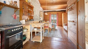L’intérieur chaleureux d’un chalet comprend un coin cuisine équipé d’un poêle, de placards en bois et d’une table à manger.