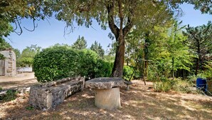 Un banc en pierre dans un jardin, avec un arbre et un mur en pierre.