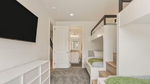 Ein schmaler Flur mit einem an der linken Wand befestigten Fernseher, einer Treppe auf der rechten Seite und einer Tür zum Badezimmer.