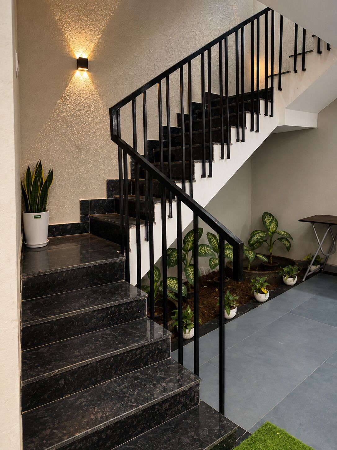 A staircase with black railings, a wall-mounted light, and potted plants.