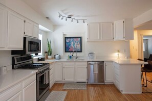 A modern kitchen with white cabinetry, a stainless steel refrigerator, a microwave, and a gas stove. - Executive Sloan’s Lake Charmer (Denver)