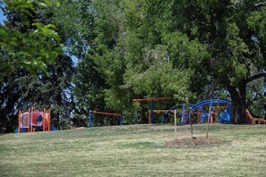 A playground with swings and climbing structures, surrounded by trees. - Executive Sloan’s Lake Charmer (Denver)