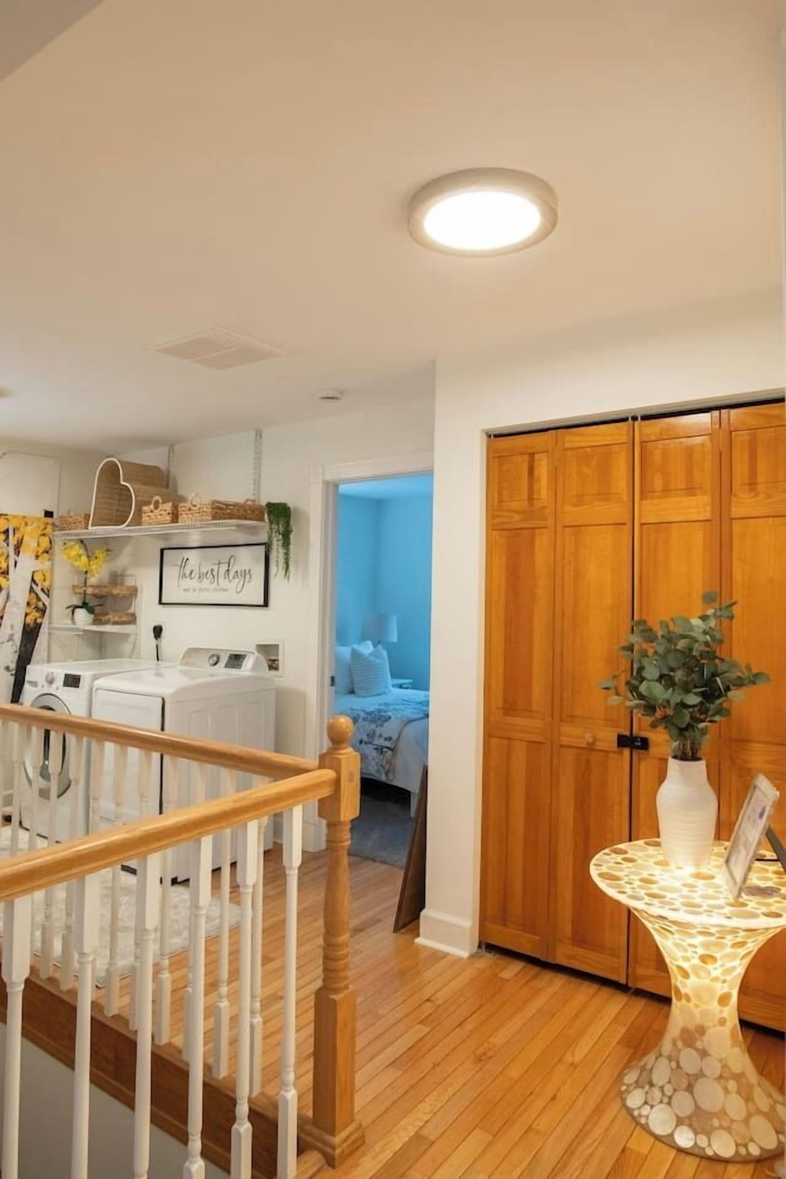 A staircase leading to a bedroom with a wooden floor, a round table with a vase, and a wardrobe with a plant.