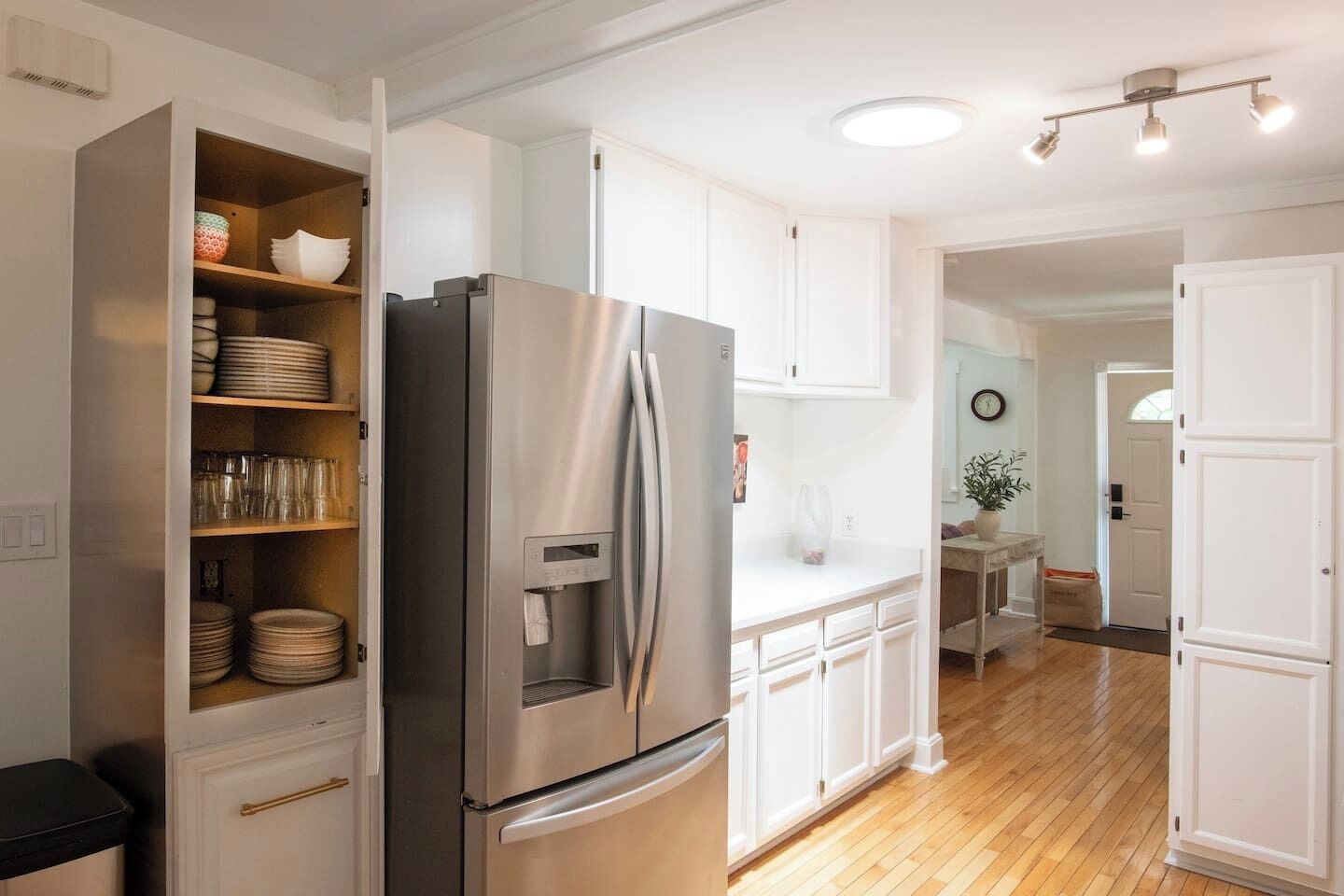 Una cocina moderna con armarios blancos, un refrigerador de acero inoxidable y piso de madera.