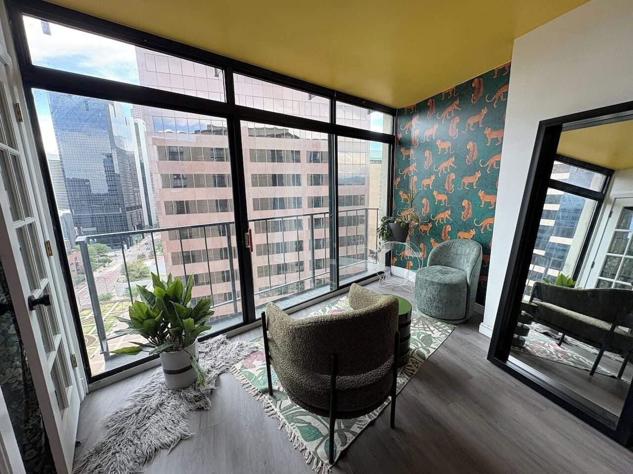 A spacious balcony with a view of city buildings, a round chair, a potted plant, and a patterned wall.