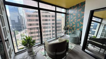A spacious balcony with a view of city buildings, a round chair, a potted plant, and a patterned wall.