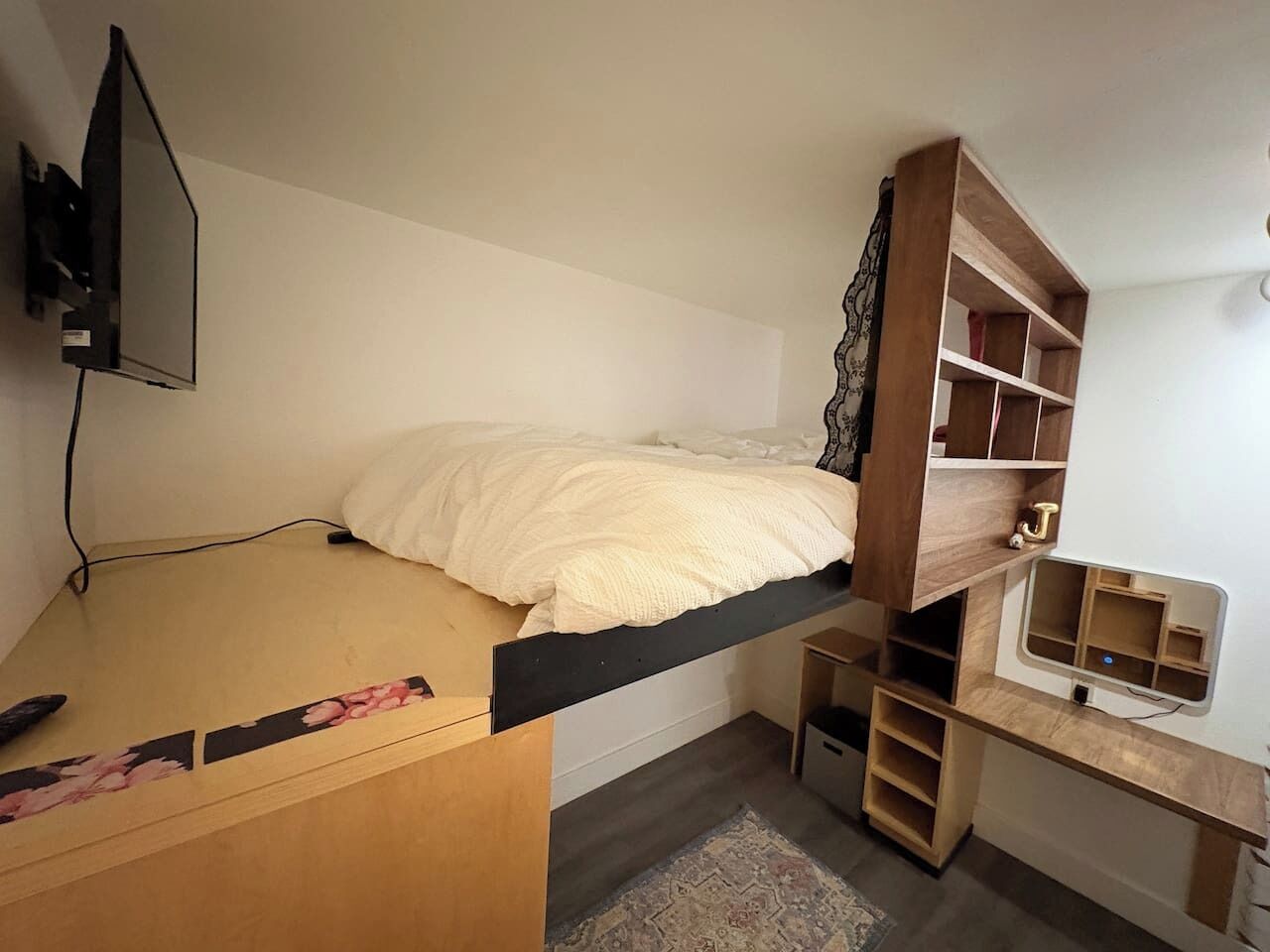A bunk bed with a desk and shelving unit, a television mounted on the wall, and a patterned rug on the floor.