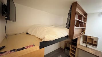 A bunk bed with a desk and shelving unit, a television mounted on the wall, and a patterned rug on the floor.