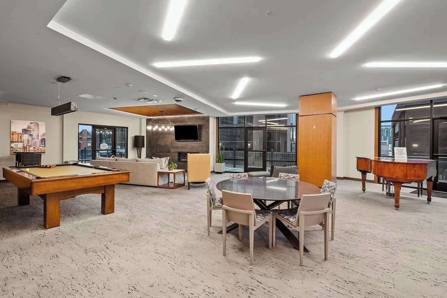 A modern lounge area with a pool table, a round table with chairs, a sofa, and a piano.
