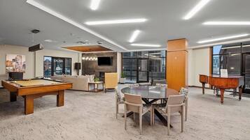 A modern lounge area with a pool table, a round table with chairs, a sofa, and a piano.