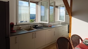 A kitchen with a large window, wooden beams, and a dining area with wicker chairs.