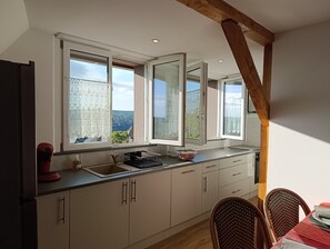 A kitchen with a large window, wooden beams, and a dining area with wicker chairs.