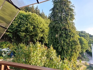 A balcony with a view of dense greenery and a tall tree.