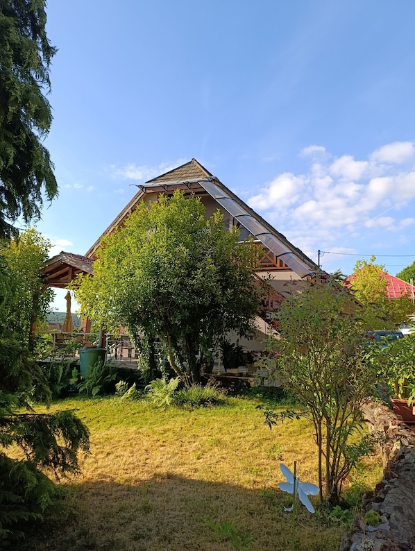 A house with a sloped roof, a pergola, and a garden with various plants and a butterfly sculpture.