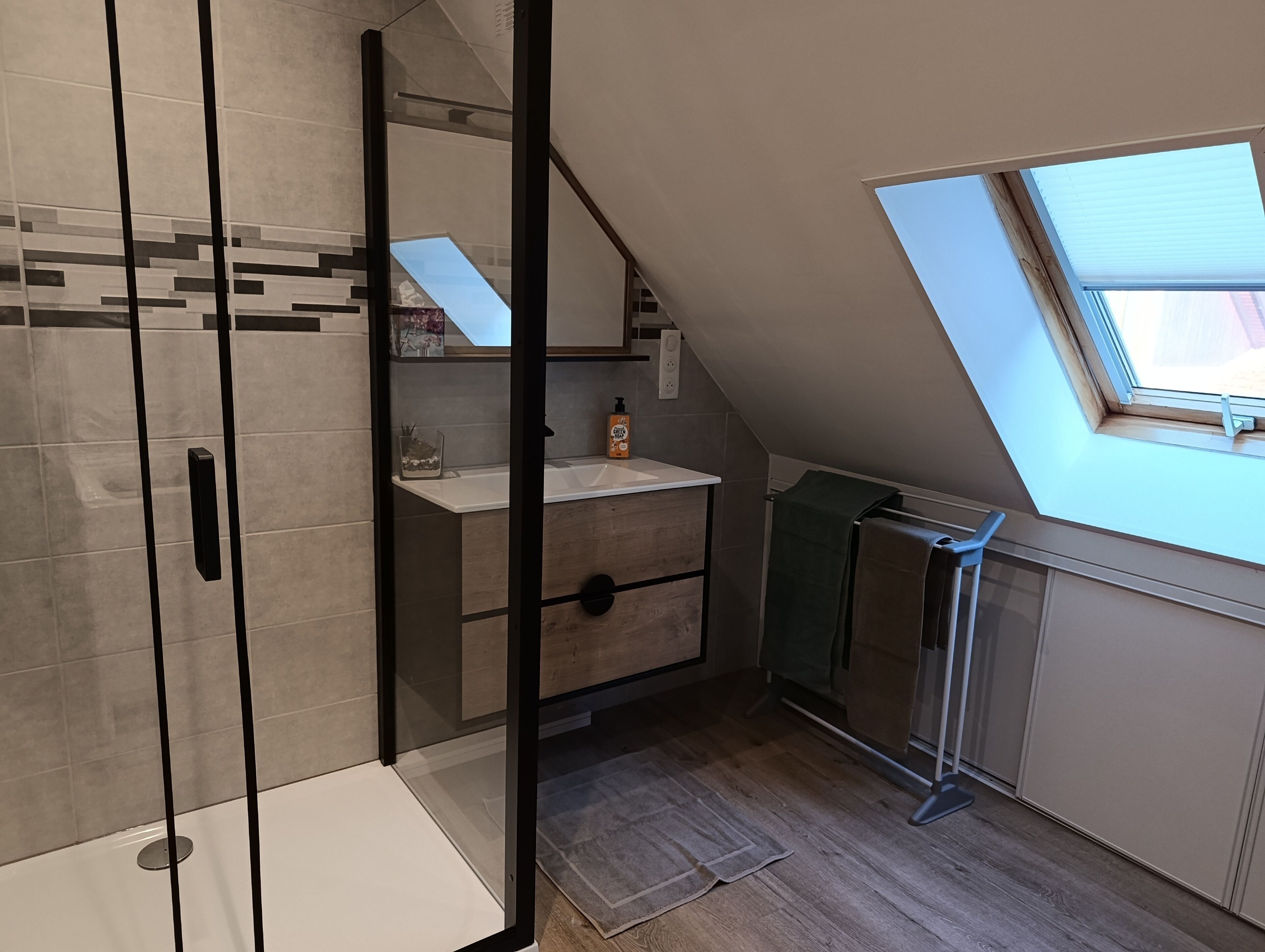 Une salle de bain moderne avec une douche à parois de verre, un meuble-lavabo en bois et un puits de lumière.