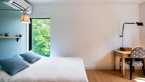 Een slaapkamer met een bed, een bureau, een stoel, een raam en een airconditioning.