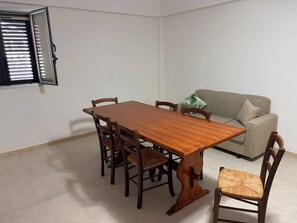 Een zithoek met een houten tafel en stoelen, een bank en een raam met zonwering.