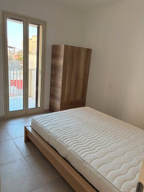 A bedroom with a bed, a wooden wardrobe, and a sliding glass door to the outside. - Apartment in a Villa, 30 meters from the beach (Agnone)