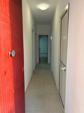 A hallway with a red door on the left, white walls, and a light fixture on the ceiling. - Apartment in a Villa, 30 meters from the beach (Agnone)