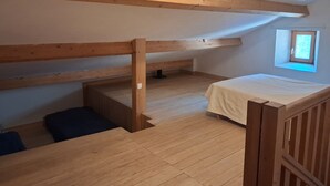 Slaapkamer in een loft met zichtbare houten balken, een klein raam en een bed.