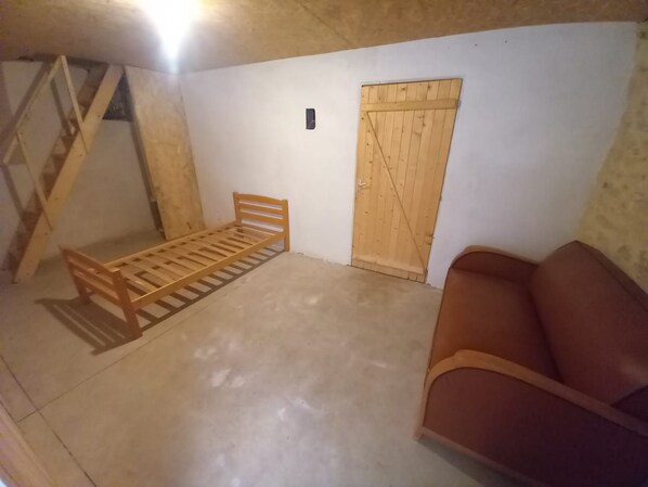 Quarto com cama de madeira, uma cadeira marrom, porta de madeira e escada.