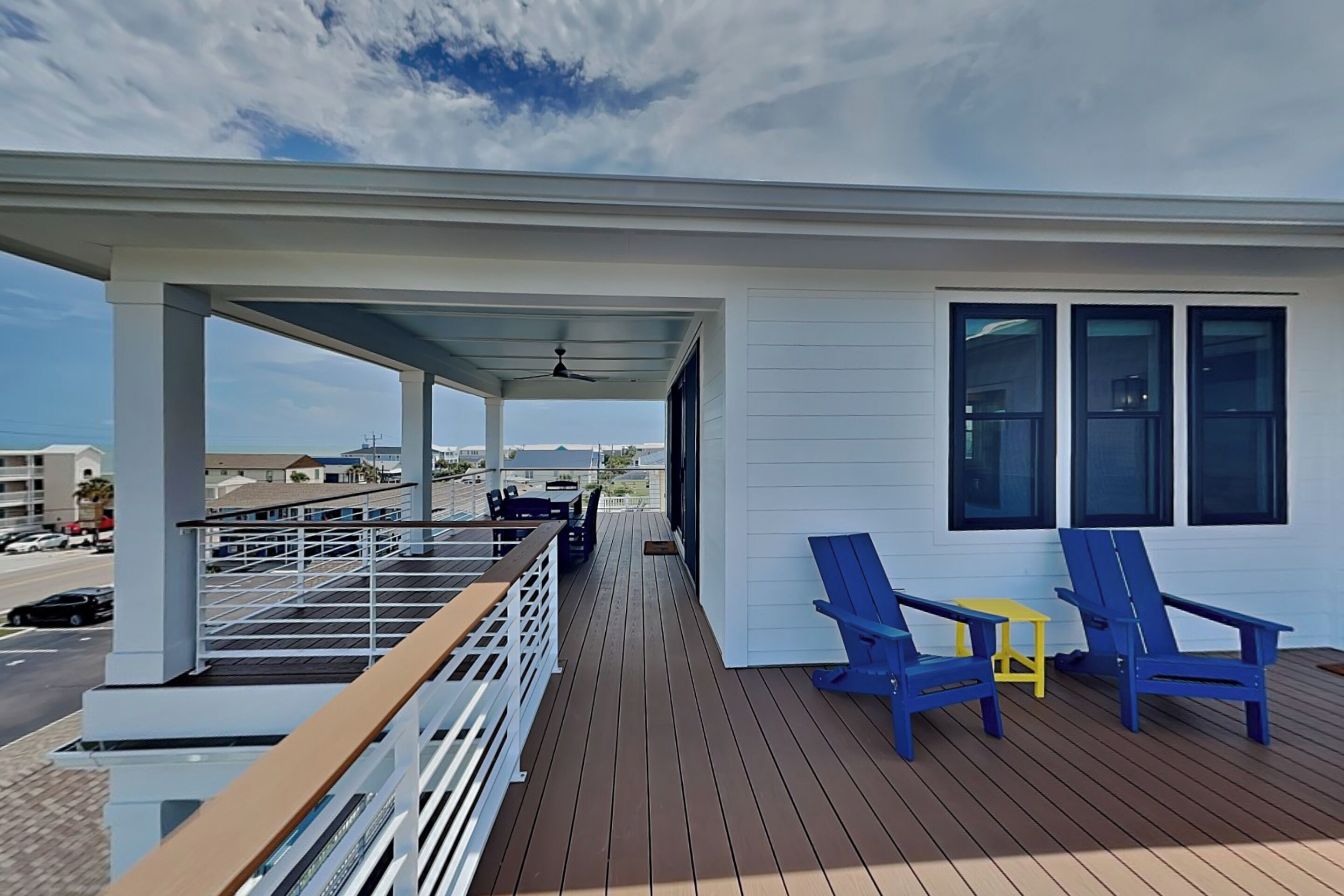 A covered outdoor deck with a railing, a table, and two chairs.