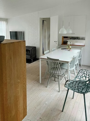 A modern kitchen with white cabinets, a dining table with chairs, and a built-in oven. - Architect-designed cottage where sea meets forest (Haverdal)