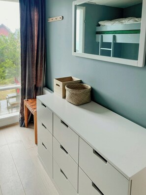 A room with a bunk bed, a wooden bench, a white dresser with drawers, and a window with curtains. - Architect-designed cottage where sea meets forest (Haverdal)