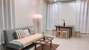 A modern living room with a sofa, a coffee table, a dining table with chairs, and a floor lamp. - 1BR Apartment Beach Getaway Perfect for Couples (San Fernando)