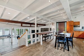 A spacious indoor area with a wooden bench, dining table, and chairs, a staircase with white railings, and a kitchen area with wooden cabinets. - Relaxing Badin Lake Waterfront l Private Pier,Hot Tub,Pool Table-Dock Your Boat! (New London)