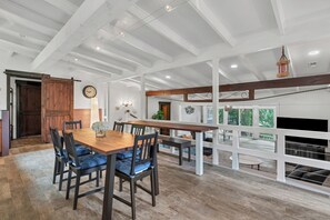 A spacious dining area with a wooden table and chairs, a clock on the wall, and a view of the outdoors through large windows. - Relaxing Badin Lake Waterfront l Private Pier,Hot Tub,Pool Table-Dock Your Boat! (New London)