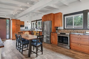A modern kitchen with wooden cabinets, stainless steel appliances, and a large dining table. - Relaxing Badin Lake Waterfront l Private Pier,Hot Tub,Pool Table-Dock Your Boat! (New London)