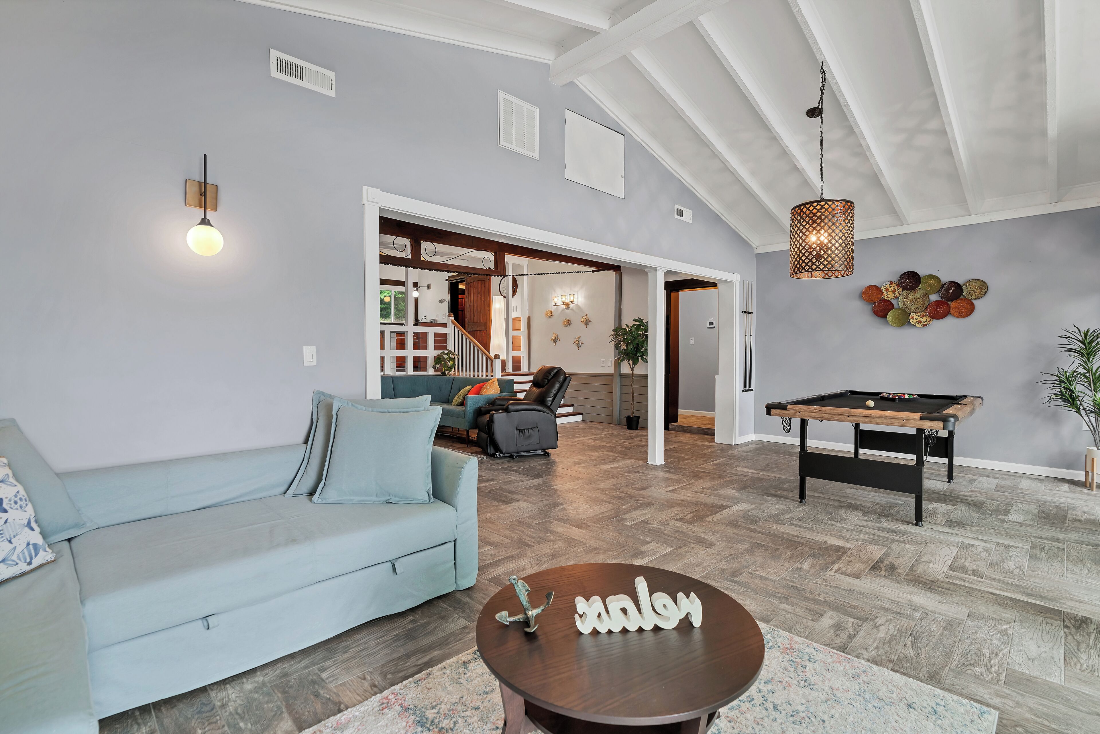 A spacious living room with a light blue sofa, a pool table, and a wooden coffee table with a decorative item.
